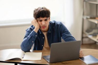 Mutsuz, aşırı çalışan Arap işadamı üzgün bir şekilde işyerinde oturuyor ve ofisin içindeki dizüstü bilgisayara bakıyor. İş konularında iş sorunları ve hatalar
