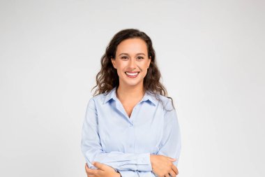 Gülümseyen genç Avrupalı kadın kendini kucaklıyor, savunmasız bir şekilde. Kollar sımsıkı sarılıyor, elle tutulur bir güvensizlik ve duygusal karışıklığa karşı rahatlık ve koruma yaratıyor.