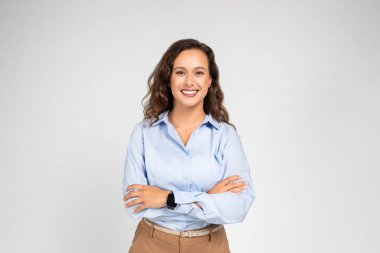 Gülümseyen sakin Avrupalı iş kadını, kollarını kavuşturmuş resmi giyinen öğretmen, arka plandaki gri arka plan stüdyosunda izole edilmiş. İş, eğitim, reklam ve teklif