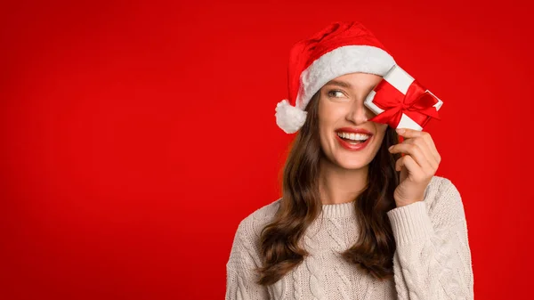 ヨーロッパの若い女性は 少し包まれたクリスマスプレゼントでポーズし 赤いスタジオの背景にギフトボックスで目を覆います お祝いの季節を与える贈り物の喜びと期待 パノラマ フリースペース — ストック写真
