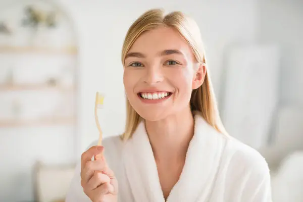 Perfect Smile. Happy Young Blonde Woman Posing With Toothbrush Brushing Teeth Looking At Camera In Modern Bathroom Indoors. Oral Hygiene Routine, Toothpaste And Toothcare Products Advertisement