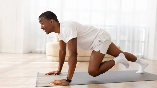 stock image Active african american young man doing cardio exercises for healthier living during home workout. Black guy leading sporty lifestyle, training in living room interior, copy space, panorama