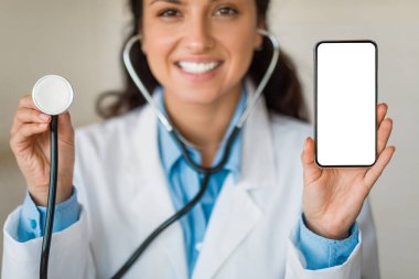Bir elinde steteskop, diğer elinde boş bir akıllı telefon olan beyaz önlüklü neşeli kadın doktorların yakın çekimi.