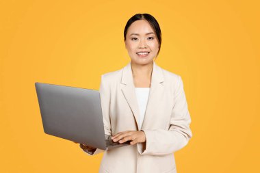 Neşeli, kendine güvenen bin yıllık takım elbiseli Koreli bayan dizüstü bilgisayarda yazıyor, sohbetin, pazarlamanın, turuncu stüdyo arka planında izole olmanın tadını çıkarıyor. İş, eğitim ve uzaktan kumandayla iş.