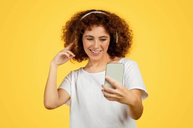 Mutlu Avrupalı genç kadın, kablosuz kulaklıklarda müzik dinle, neşeni ifade et, telefonda, sarı arka planda video izle. Boş vakitte dans et, online ders, video uygulaması