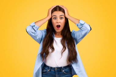 Ağzı açık, kafası ellerle tutulmuş, stres ve basınçtan muzdarip, sarı arka planda izole edilmiş Avrupalı genç bir bayan. Çalışırken çok çalışmak, sınava hazırlanmak, işte sorunlar.