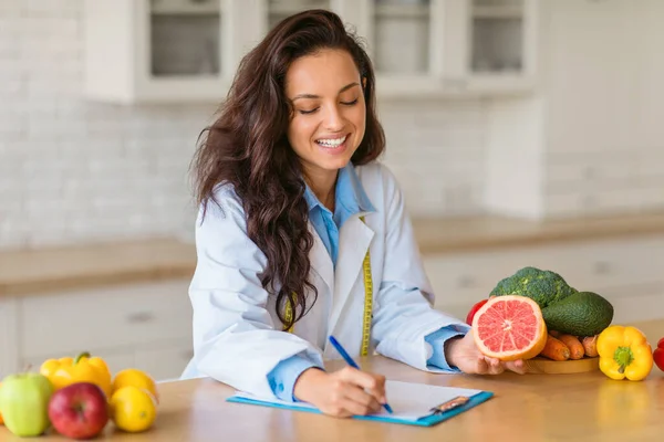 Smiling Nutritionist Lab Coat Writes Clipboard Showcasing Sliced Grapefruit Assorted — Stock Photo, Image