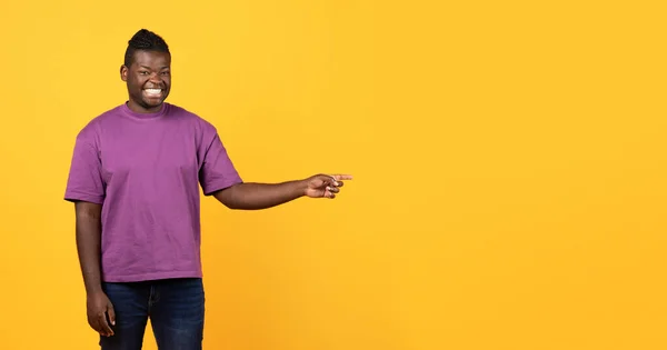 微笑的非裔美国人指出手指以外在免费的空间广告提供 微笑的相机站在黄色的背景 看那里概念 工作室拍摄 — 图库照片