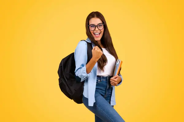 快乐而聪明的女学生戴着眼镜背着背包 享受着成功 在黄色的工作室背景下与世隔绝 教育和学习 学校生活方式 — 图库照片