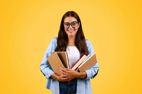 戴眼镜的年轻快乐的女学生手里拿着很多书 都是黄色的画室背景 教育的享受 学习和作业 学校生活方式 广告和提供 — 图库照片