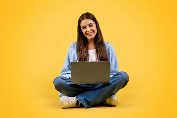 积极的高加索女学生使用笔记本电脑 工作和坐在地板上 隔离在黄色背景 工作室 在线学习 教育和远程授课 — 图库照片