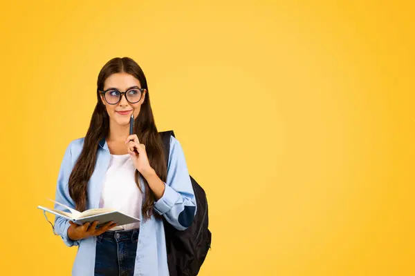 沉思快乐的女学生 戴着眼镜 背着背包 计划学习日 孤立在黄色的工作室背景下 学校教育的选择 生活方式和项目 广告和提供 — 图库照片
