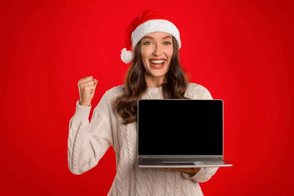 特別なオンラインクリスマスオファー ラップトップコンピュータでポーズし Yesをジェスチャーし 赤い背景の上に空のスクリーンモックアップを示すエキサイティングな女性 Xmasでの優れたEコマース販売 — ストック写真