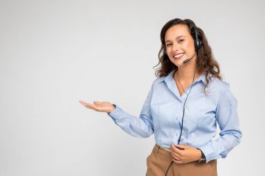 Resmi kıyafet ve kulaklıkla gülümseyen genç Avrupalı bayan danışma müşterisi, el ele boş alan, arka plandaki gri arka planda izole edilmiş. Mesleki tavsiye, destek