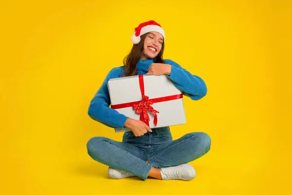 Young Woman Sits Holding Christmas Gift Box Yellow Studio Background — Stock Photo, Image