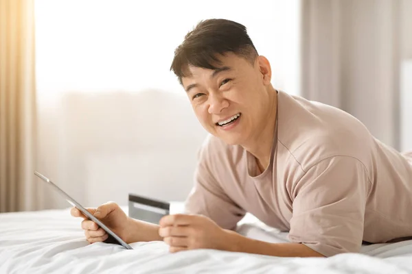 Счастливый Зрелый Азиат Пользуется Мобильным Банкингом Кредитной Картой Лежащей Кровати — стоковое фото
