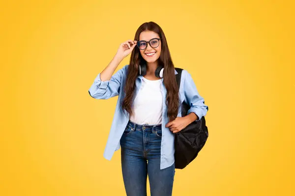高兴漂亮聪明的年轻女学生背着眼镜 享受在黄色工作室背景下孤立的课程项目 教育和学习 学校生活方式 广告和提供 — 图库照片
