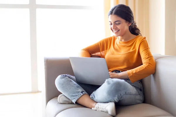 自宅で働く若いインドのフリーランサーの女性笑顔 ソファに座って コンピュータ上でインターネットをサーフィン オンラインショッピングや電子メールに返信 彼女の週末を楽しんで — ストック写真