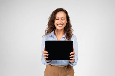 Gri stüdyo arka planında izole edilmiş, boş alanı olan Avrupalı genç kadın profesyonel gösteri tableti. İş dikkati, iş uzaktan kumanda, alet tavsiyesi, reklam ve teklif