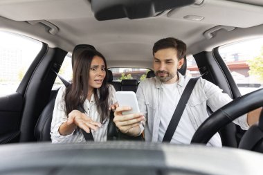 Kızgın, genç bir kadın el kol hareketi yapıp bağırırken kocası araba şoförü olan adam cep telefonu kullanıyor ve konsantrasyonunu kaybediyor. Tehlikeli sürüş ve aletler