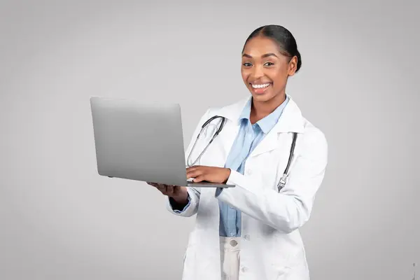 Beyaz Önlüklü Neşeli Siyah Kadın Doktor Dizüstü Bilgisayarda Yazıyor Gri — Stok fotoğraf