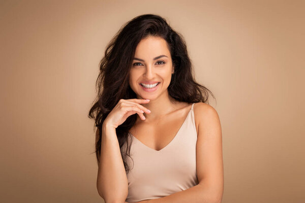 Веселая брюнетка тысячелетнего Среднего Востока женщина демонстрирует свою природную красоту в изящной позе на бесшовном студийном фоне, показывая красивую кожу и длинные волосы