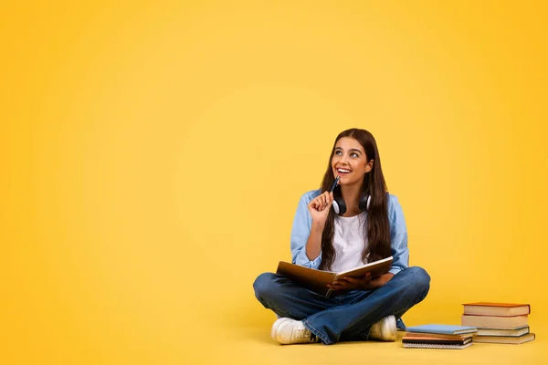 积极沉思的女学生 带着书本 坐在地板上 看着复制的空间 孤立在黄色的工作室背景下 学校教育选择 生活方式和规划项目 — 图库照片
