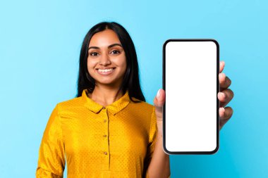 Büyük, boş ekranlı, mobil uygulama gösteren ya da mavi stüdyo arka planında poz veren mutlu Hintli kadın. Modern teknoloji iletişim konsepti