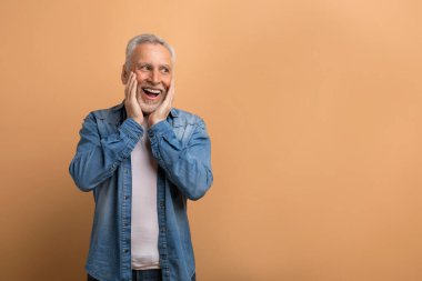 60 yaşında, bej arka planda duran yakışıklı bir adam. Şaşırmış kıdemli bir adamın portresi reklam ürünleri ve hizmetler, fotokopi alanına bakmak, yüzlere dokunmak