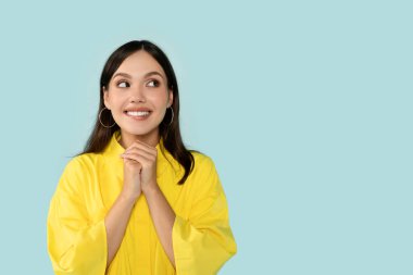 Heyecanlı, esmer, İspanyol asıllı genç bir bayan, el ele tutuşmuş, metin ya da reklam için fotokopi odasına bakıyor ve gülümsüyor, güzel bir anlaşma yapıyor, mavi arka planda izole edilmiş.