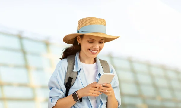 陽気なミレニアル世代の白人女性観光客バックパックで帽子をかぶり 電話で入力し オンラインマップ チャットを使用します チケット 夏休みのアクティブライフスタイル ガジェット 旅行ブログ — ストック写真