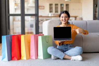 İnternetten alışveriş. Evde alışveriş poşetlerinin yanında boş ekranla dizüstü bilgisayarı gösteren, Doğulu Kadın İnternet alışverişi için web sitesi öneren,