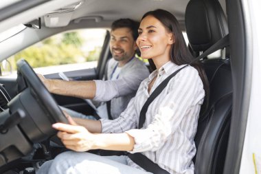 Gülümseyen esmer kadın sürücü kursunda park pratiği yapıyor, yakışıklı eğitmenle arabada oturuyor. Neşeli milenyum adamı araba kullanan koç bayan öğrenciye araba kullanmasında yardım ediyor.