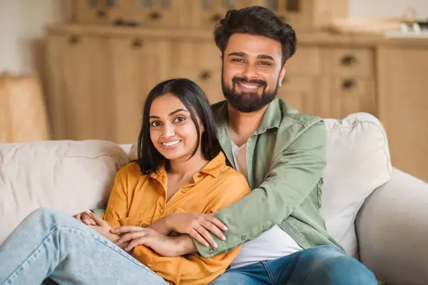 Young Hindu spouses displaying affection while seated on couch at home, their close proximity and genuine smiles signify loving and supportive relationship, radiating warmth and happiness