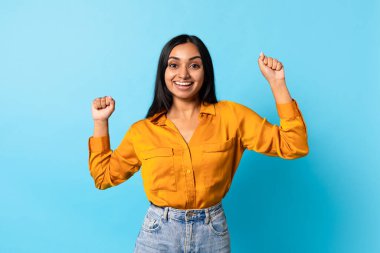Gülümseyen Hindu milenyum bayanı zaferle el sıkışırken mavi stüdyo arka planında duruyor. Kazanan başarıyı kutluyor, neşe ve zafer ifade ediyor, reklam başarısı