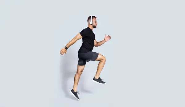ワイヤレスヘッドフォン スポーツウェアリスニングミュージック ランニング ジャンプ 空気中の凍結 灰色のスタジオの背景に隔離されたミレニアムヨーロッパの男 ボディケア スポーツ カーディオトレーニング — ストック写真