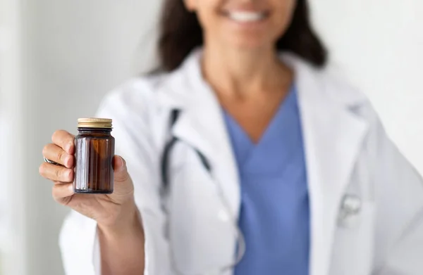 Cropped of woman doctor holding glass jar with pills in her hand close-up. Unrecognizable doc reminds about taking medicine for health support. Drugs, medication, vitamins and supplements
