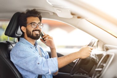 Neşeli milenyum Hindistanlı adam yeni araba sürüyor ve telefonla arkadaşından sevgilisine sesleniyor, otomobilin içinde akıllı telefondan konuşuyor, cep telefonuyla konuşan sürücüyü yan görüyor.
