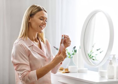 Güzel Ortaçağ Kadın Açılış Şişe Evde Yüzü Serum, Çekici Olgun Kadın Yeni Kozmetik Ürünler Kullanıyor, Giyinme Masasında Oturuyor, Evcil Güzellik Rutininin keyfini çıkarıyor
