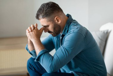 Oturma odasındaki koltukta oturan bunalımlı orta yaşlı bir adam. Kafasını kaldırmıyor, zihinsel sağlık ve mali sorunları var. Evde yalnızlıktan muzdarip bir adamın yan görünüşü.