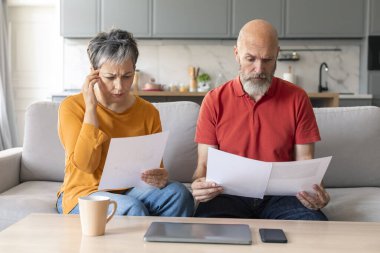 Finansal kriz. Stresli Üst Düzey Çiftler Evlerinde Belgeleri Kontrol Etme, Hayal kırıklığına uğramış yaşlı eşler Koltukta oturuyor ve banka evraklarını tutuyor, Aile Bütçesi Yönetimi ile ilgili sorunlar yaşıyor,