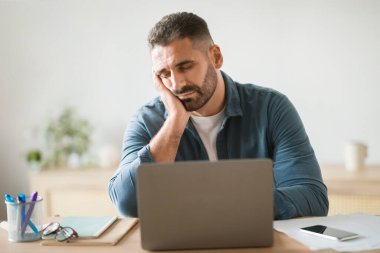 Çok çalışıyorum. Uykulu ve yorgun orta yaşlı iş adamı dizüstü bilgisayarın yanında uyuyor, çevrimiçi çalışmaktan yorulmuş ve sıkılmış, modern ofis içi çalışma masasında oturuyor. İşkolik Yanık