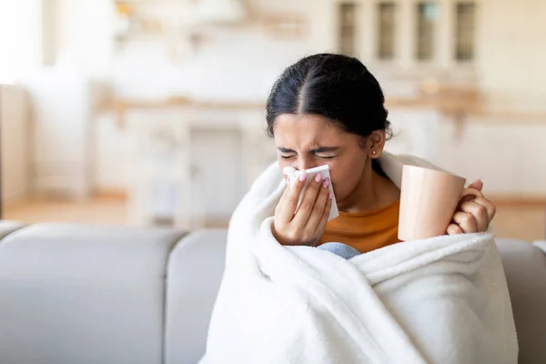 風邪とインフルエンザの症状 病気の若いインドの女性は リビングルームでソファに座っている間 彼女のランニング鼻を吹き飛ばす毛布で覆われ お茶を飲んで 自宅で気分が悪くなる — ストック写真