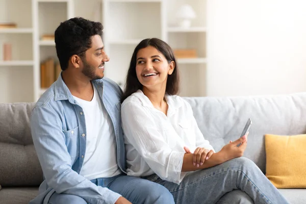 Young loving Indian couple shares light-hearted moment, smiling and engaging with each other while woman holds smartphone, reflecting their bond and modern lifestyle