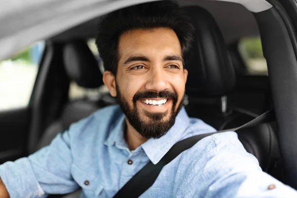 Cheerful indian man driving car, shot from outside, going on trip during vacation, side view, copy space. Happy indian guy in casual outfit driving his brand new nice car, closeup