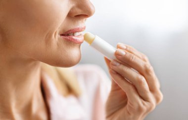 Dudak kremi. Tanımlanamayan orta yaşlı bir kadın dudaklarına nemlendirici sürerken olgun bir kadının nemlendirici dudak kremi sürerken evde güzellik rutini yaparken görüntüsü kesiliyor.