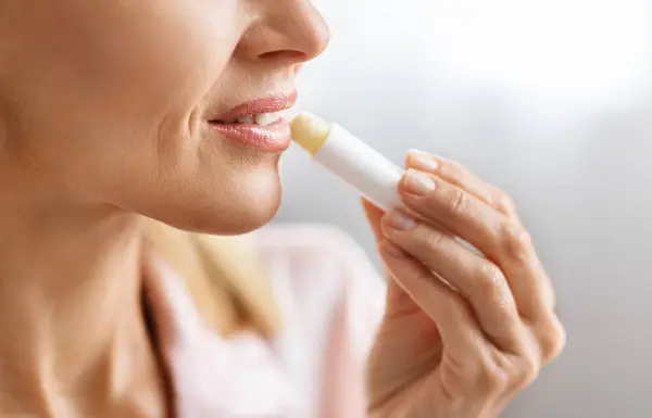 Lip Care. Unrecognizable middle aged woman applying moisturising chapstick on lips, cropped image of mature female using nourishing lip balm while making beauty routine at home, closeup