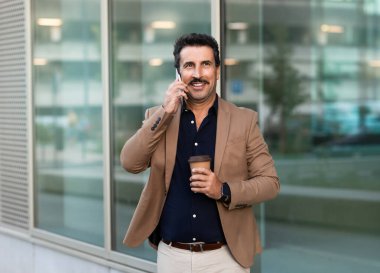 Orta Doğulu işadamı sokakta yürürken telefonla konuşuyor, elinde hazır kahveyle. Mutlu başarılı girişimci öğle arasında dışarıda fotokopi alanına bakarak iş görüşmesi yapar.
