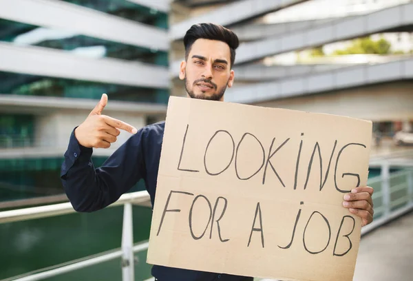 一个阿拉伯商人指着纸签 上面写着 寻找工作 摆出一副城市建筑的架势 搜索着工作清单 金融危机期间的失业和公司裁员 — 图库照片