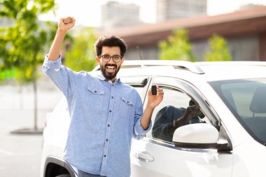 Duygusal yakışıklı Hintli adam elini kaldırıyor ve kameraya gülümsüyor. Yepyeni beyaz arabasının anahtarını gösteriyor. Kopya alanı. Bin yıllık zengin Hindu adam dışarıdaki lüks galeride araba satın alıyor.